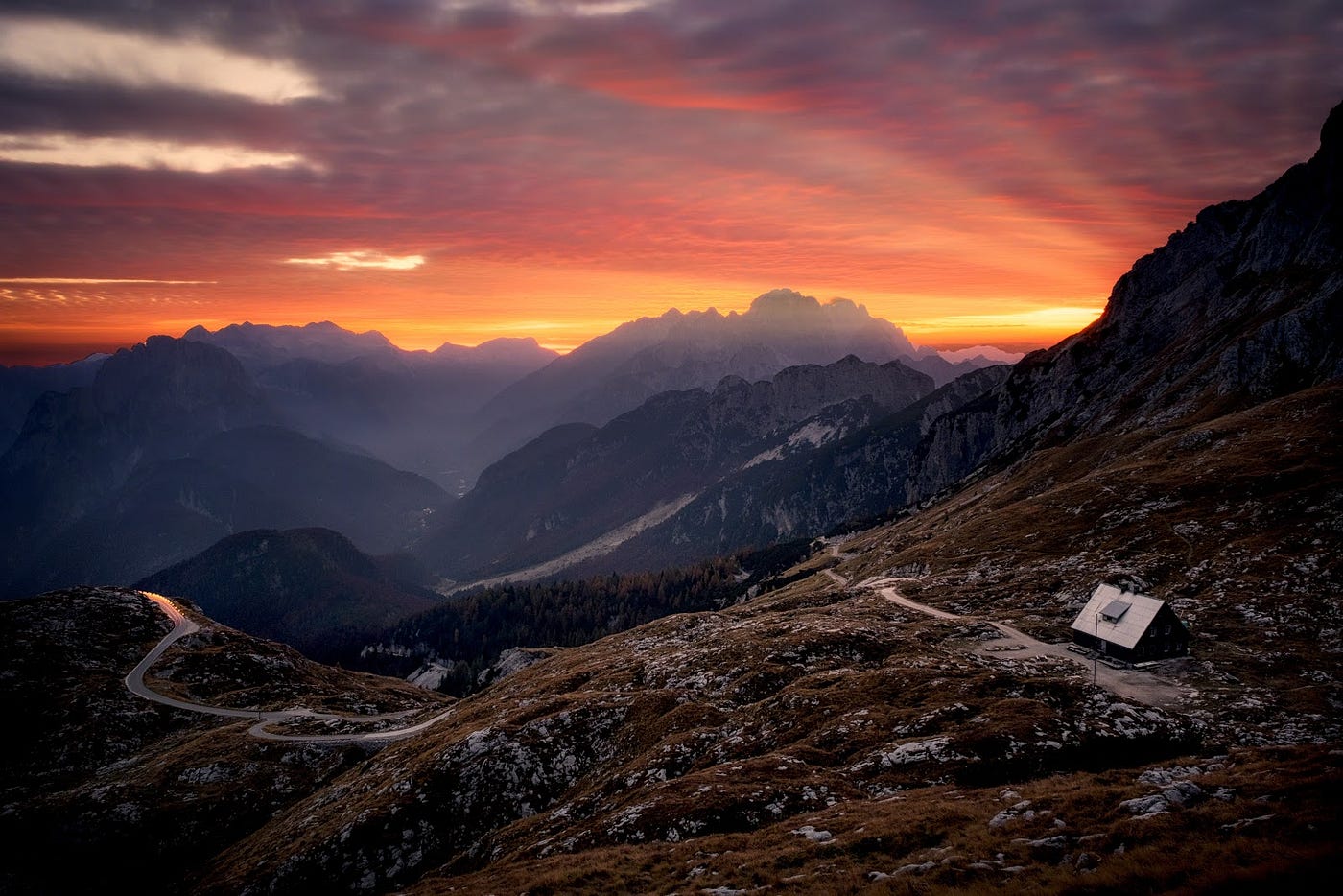 Colorful sunset over a road winding through rocky mountains.